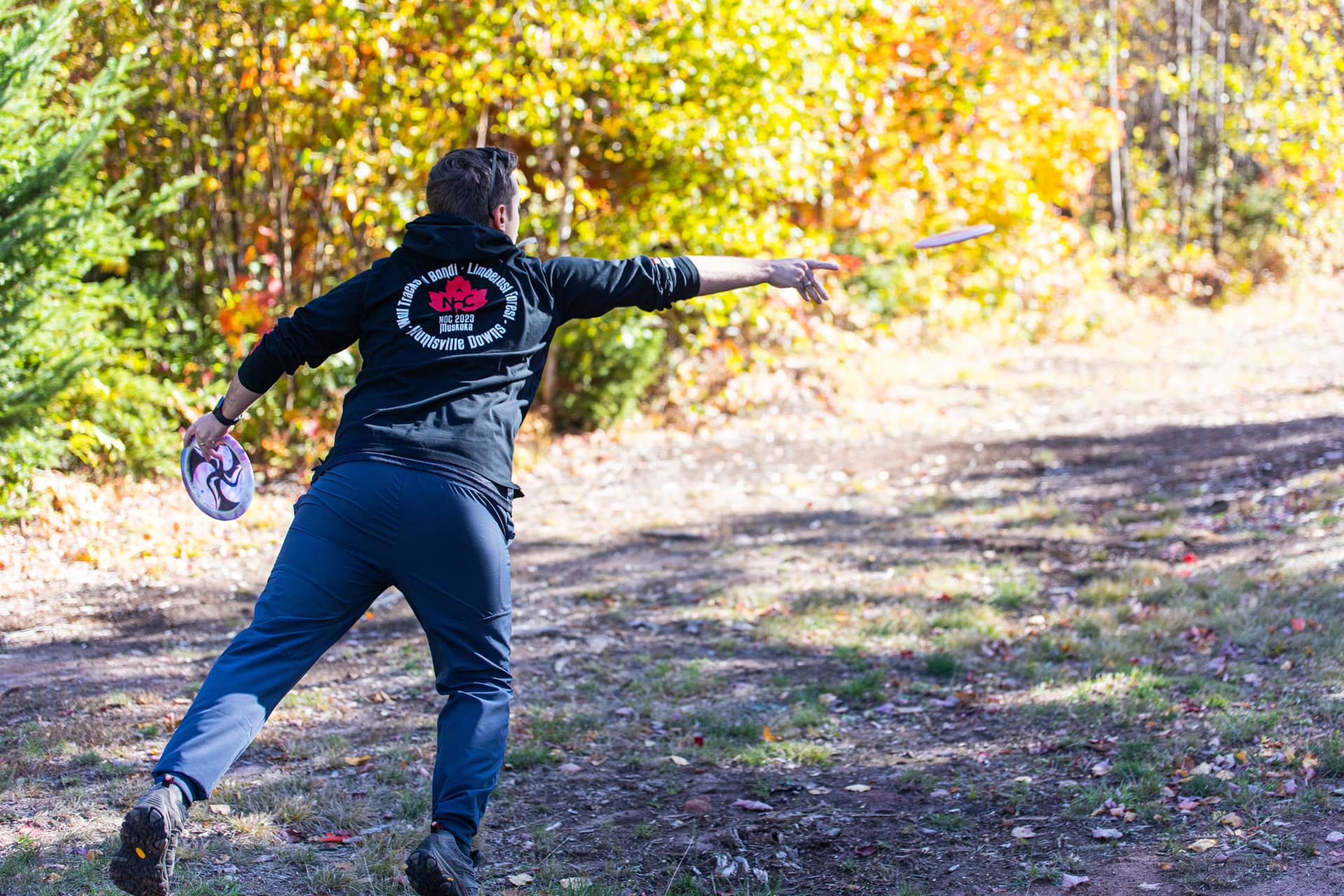 Mid-release down a leaf-covered wooded fairway in tournament gear